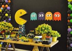 a table topped with lots of food and balloons in the shape of pacman faces