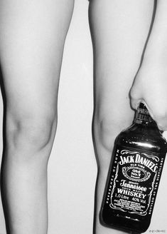 black and white photograph of legs with jack daniels bottle on the bottom right leg, from behind