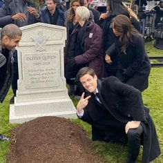 a man kneeling down in front of a grave with people around him looking at the ground