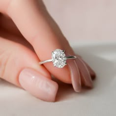 a woman's hand holding a diamond ring on her finger, with the center stone in