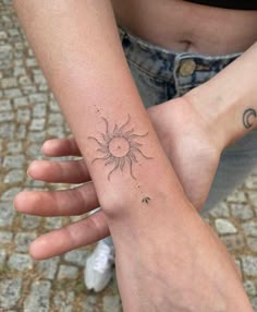 two people holding hands with tattoos on their arms and one has a sun in the middle