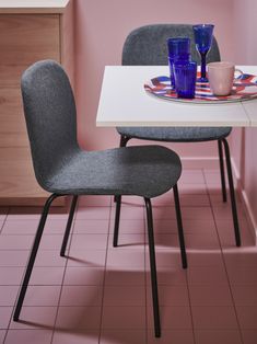 two chairs sitting at a table with plates and cups on it in a pink room