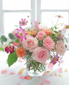 a vase filled with pink and orange flowers on top of a white table next to a window