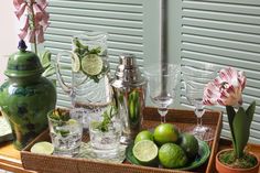 a tray filled with glasses and limes on top of a table next to flowers