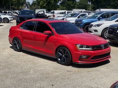 a red car parked in a parking lot next to many other cars and suvs