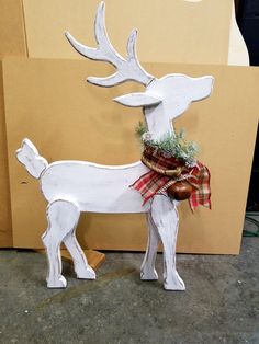 a white wooden deer with a red plaid bow on its antlers is standing in front of a cardboard box