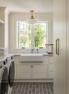 a washer and dryer in a kitchen with white cabinets, tile flooring and windows