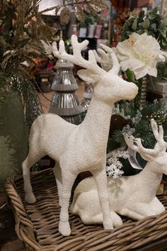 two white deer figurines sitting on top of a wicker basket next to flowers