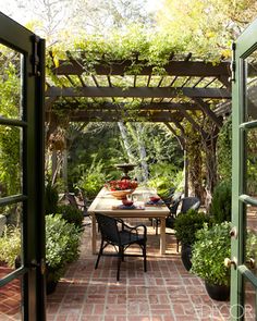 an outdoor dining area with brick flooring and potted plants on the table, surrounded by greenery