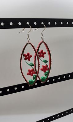 pair of red and green flower earrings hanging from hooks on black metal bar with white background