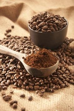 a spoon full of coffee beans next to a bowl filled with cocoa powder on a table