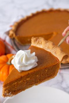 a slice of pumpkin pie being held up by a hand with whipped cream on top