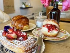 a table topped with pastries covered in powdered sugar and strawberries next to a croissant