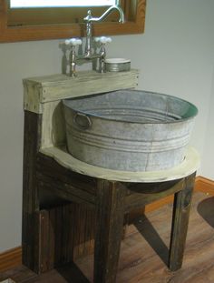 an old bucket sink sits on a wooden table in the corner of a room with a mirror above it