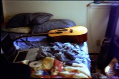 a guitar sitting on top of a bed next to a window