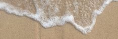 the water is foamy on the sand at the edge of the beach and it looks like waves are coming in from the shore