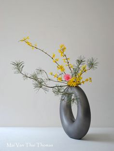 a gray vase with yellow and pink flowers in it sitting on a white table top