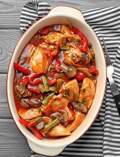 a white bowl filled with chicken and vegetables on top of a striped cloth next to a fork