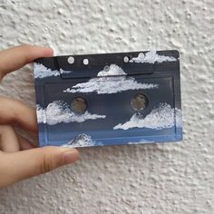 a hand holding an old fashioned cassette with clouds on the side and two eyes in the middle