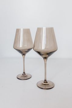 two wine glasses sitting side by side on a white surface with no one around them