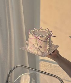 a hand holding a cake on top of a glass plate next to a white curtain