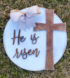 a wooden cross with the words he is risen on it and a bow hanging from it