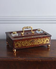 an antique wooden box with gold decorations on it sitting on a table next to a white wall