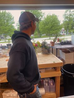 a man standing in front of a window looking out at the yard and plants outside