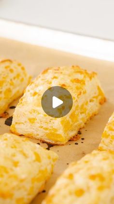 several cheesy biscuits are arranged on a piece of parchment paper with a video play button in the middle