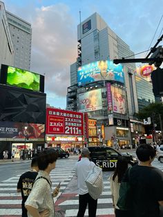 people are standing on the street in front of tall buildings and billboards at dusk