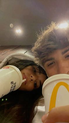 a man and woman drinking from cups in front of the camera with their faces close to each other