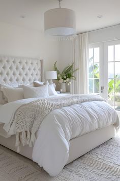 a white bedroom with a large bed and french doors leading to an outside patio area