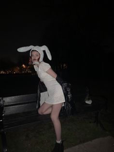 a woman dressed in bunny ears poses on a bench at night with her hands behind her head