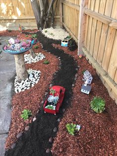 a red toy car sitting in the middle of a dirt patch next to a tree