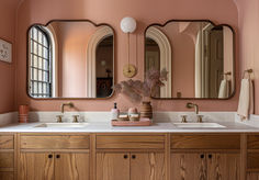 a bathroom with pink walls and two mirrors on the wall above the double sink vanity