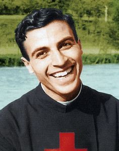 a man with a red cross on his chest smiles at the camera while standing in front of water