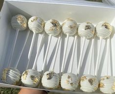 a box filled with cake pops covered in white frosting and gold sprinkles