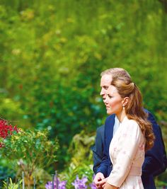 the duke and princess are looking at each other in front of some colorful flower bushes