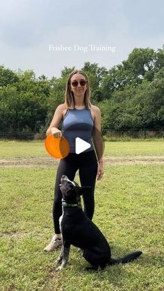 a woman holding an orange frisbee next to a black dog