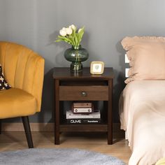 a bedroom with a bed, nightstand and chair next to each other in front of a gray wall