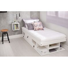 a white bed with drawers underneath it and a stool in front of the headboard