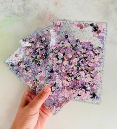 a hand is holding two coasters that have flowers on them and are covered in sequins