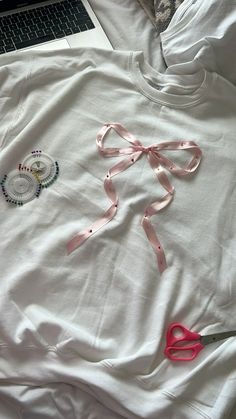 a white t - shirt with pink ribbon and scissors laying on top of it next to a laptop