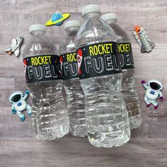 three plastic water bottles with rocket and rocket fuel labels on them, sitting next to small toy figurines