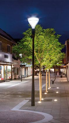 an empty city street at night with lights on and trees in the middle of it