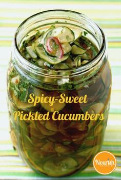 a jar filled with pickled cucumbers sitting on top of a striped table cloth