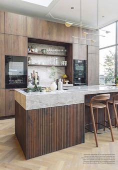 a kitchen with wooden cabinets and marble counter tops, two stools are in front of the bar