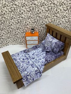 a bed with blue and white bedspread next to an orange nightstand in front of a patterned wallpaper