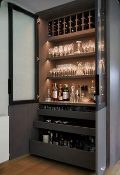 an open cabinet filled with lots of bottles and glasses on top of wooden flooring