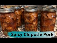 four jars filled with pickles sitting on top of a table next to a sign that says spicy chipote pork